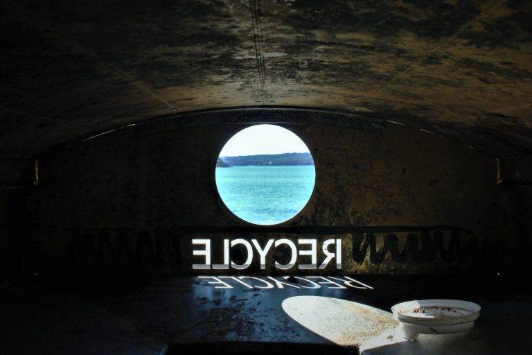 Dark room with a window to a sea, and flipped "recycle" text written on the wall